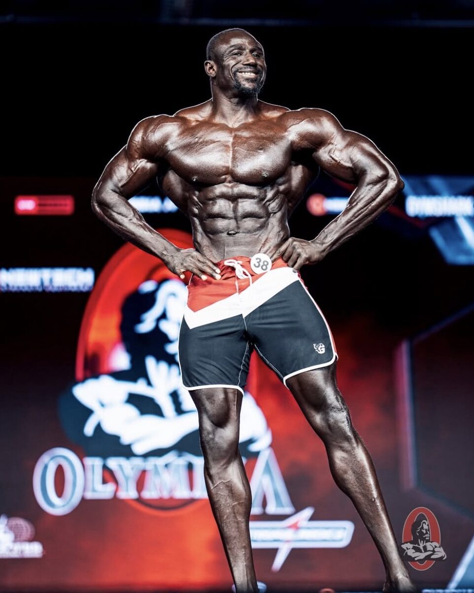 Sidy Pouye no palco do Mr. Olympia com calções Great I Am